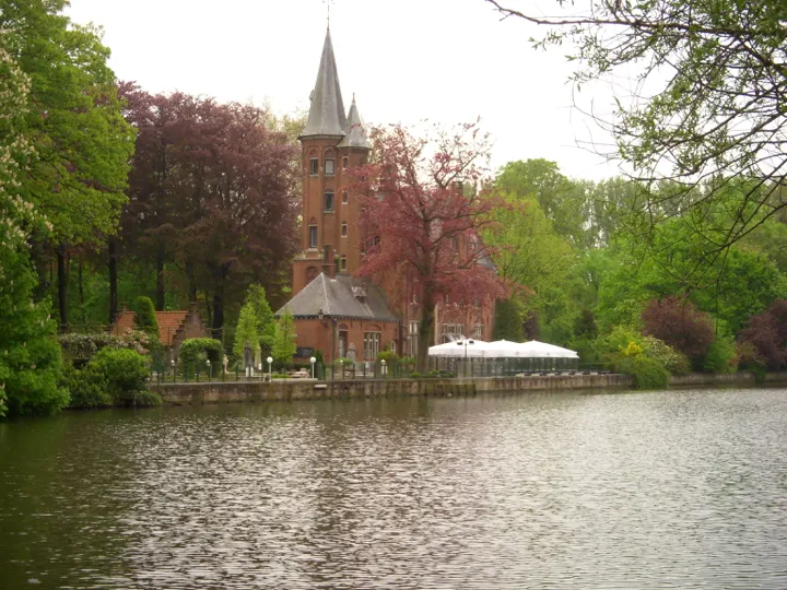 A brick tower and spire across a lake